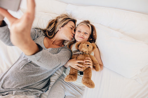 Mother and daughter taking selfie on bed