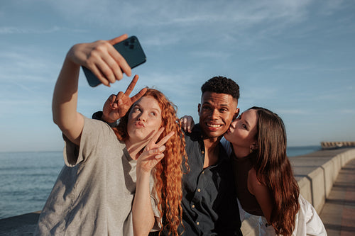 Young friends taking a group selfie next to the sea