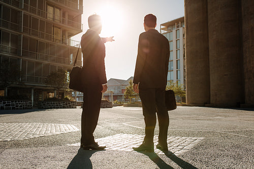 Businessman pointing towards something to colleague standing on street