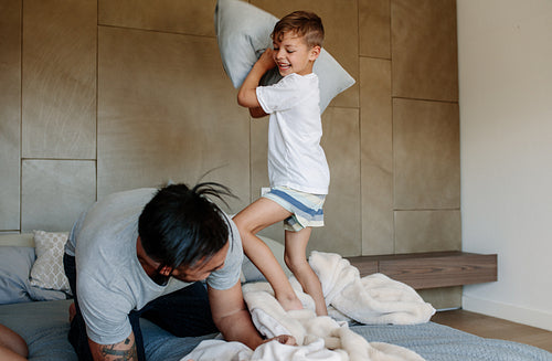 Father and son enjoying playing pillow fight in bedroom
