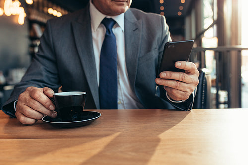Smart phone in hand of a senior businessman at cafe