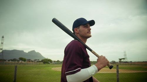 Baseball player walks across field with his bat