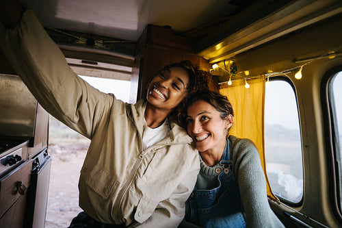 Two friends in a cozy camper share smiles while taking a selfie