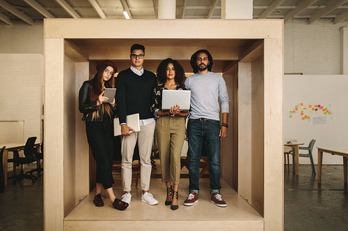 Business people standing inside a cube enclosure with laptops and tablet.