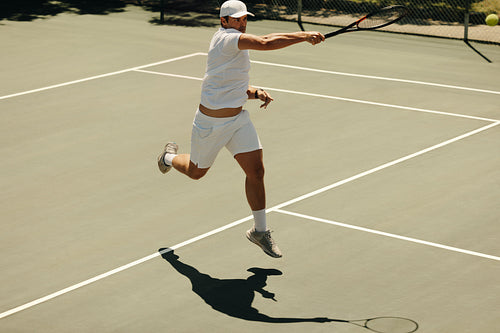 Man running and jumping on tennis court with shadow during a match