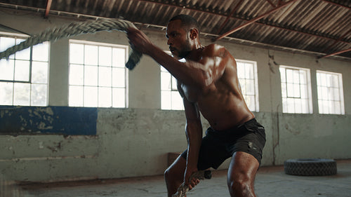Strong and muscular man working out with battle rope in gym