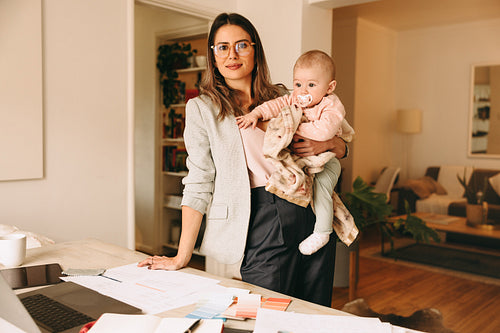 Businesswoman holding her baby while standing in her home office