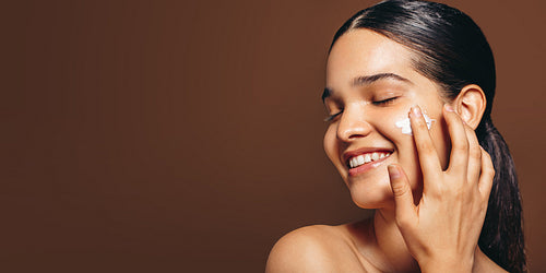 Moisturizing with face cream; young woman applies a beauty product on her clear skin