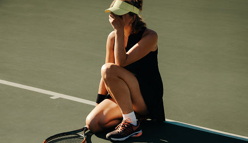 Upset woman crouched on tennis court crying after losing match