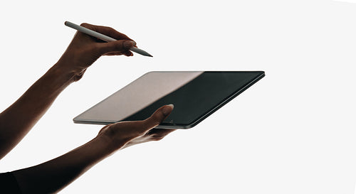 Silhouetted hands using a tablet with a stylus for digital interaction