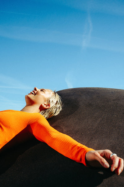 Young woman relaxes on a rock under blue sky in summer fashion