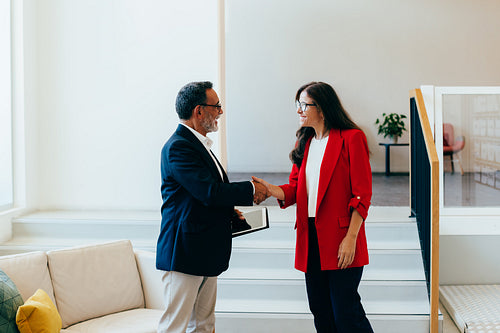 Senior management team members shaking hands professionally near a staircase
