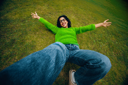 Happy woman relaxing on grass outdoors with open arms in a carefree leisure moment