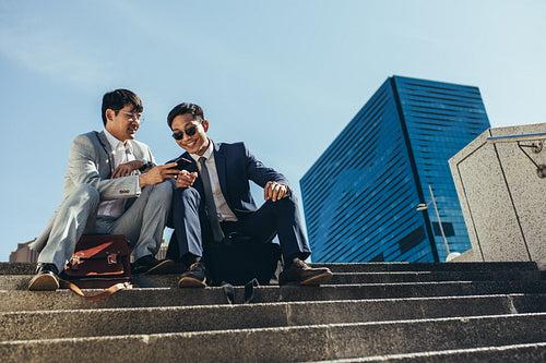 Businessmen sitting on the steps outside using smart phone