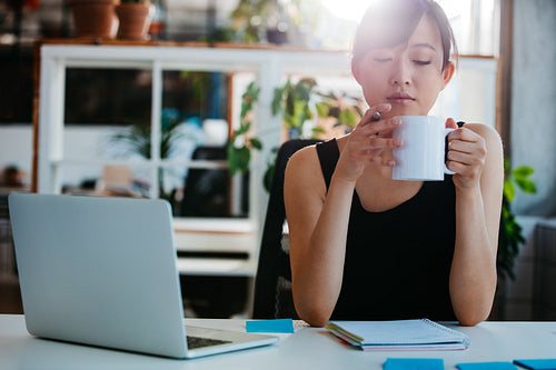 Relaxed young woman having coffee at her desk
