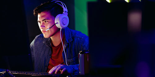 Focused on the screen, a young male player plays a video game on his computer