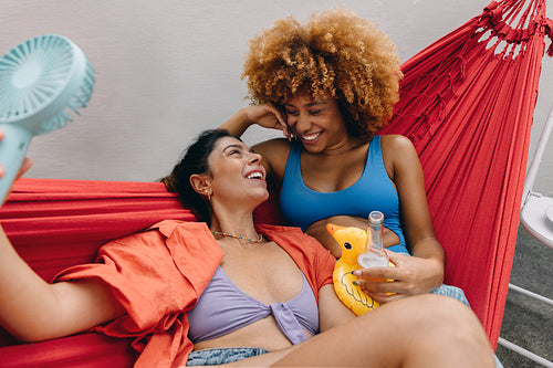 Two friends relaxing in a hammock enjoying summer weather and drinks