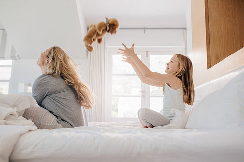 Mother and daughter playing with teddy bear on bed