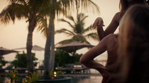 Joyful mother and daughter dancing together by the pool at sunset