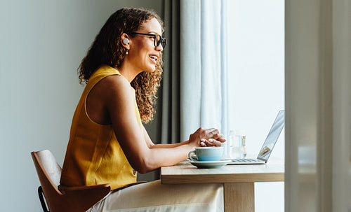 Woman video conferencing on laptop with coffee at cafe table