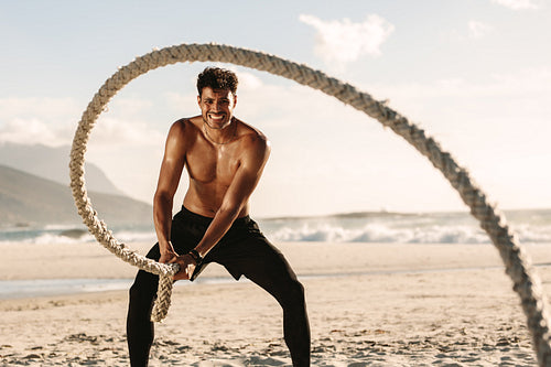 Man doing fitness training at the beach using battling rope