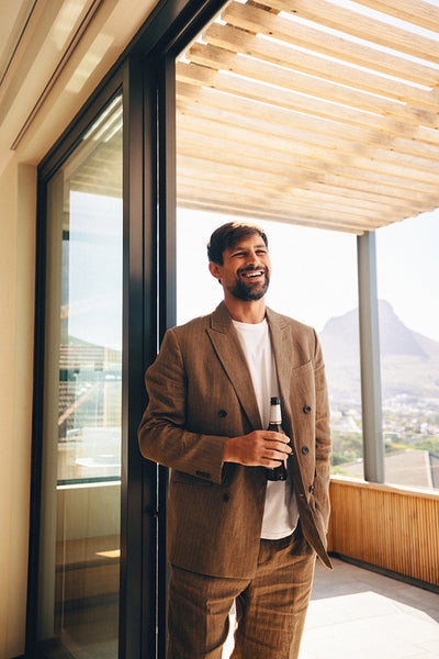 Smiling man in a casual suit holding a drink on a terrace