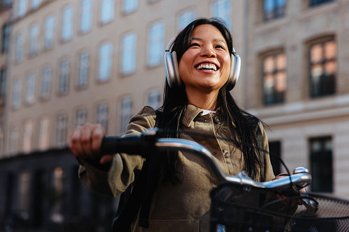 Smiling woman with bicycle and headphones in city