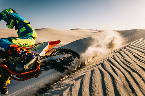 Motocross racer accelerating over sand dune