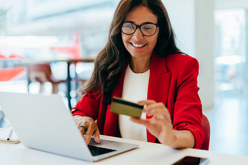 Smiling woman in red blazer using a credit card and laptop