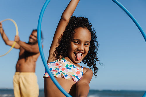 Happy girl playing with hula hoop on the beach during summer day