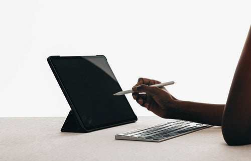 Hand using a stylus and tablet with keyboard on a clean desk
