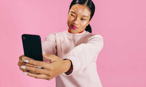 Woman taking a selfie as she flaunts her bold makeup look in a studio
