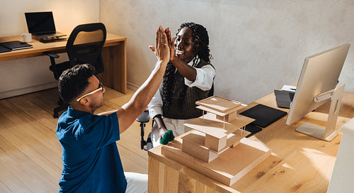 Young architects celebrating success with a high-five in a creative office setting