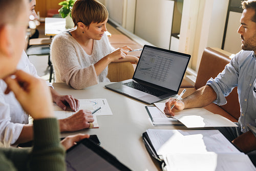 Manager showing figures on laptop to colleagues in meeting