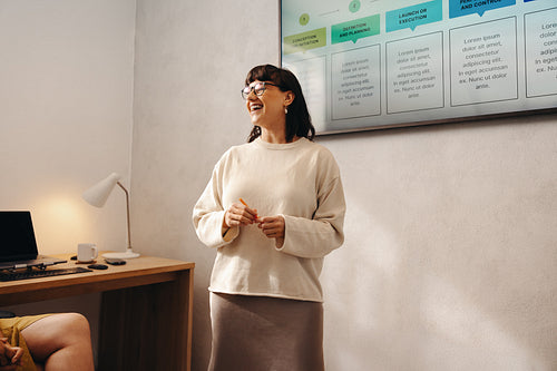 Joyful professional woman presenting during an office meeting with a large display screen