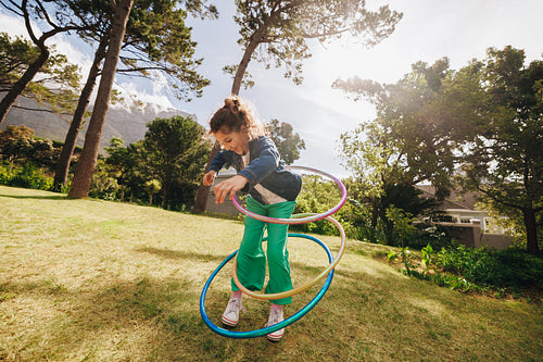 Young girl playing with colorful hula hoops in a sunny park