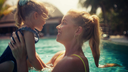 A happy mother and daughter enjoy playful splashing and bonding moments in a sunny pool