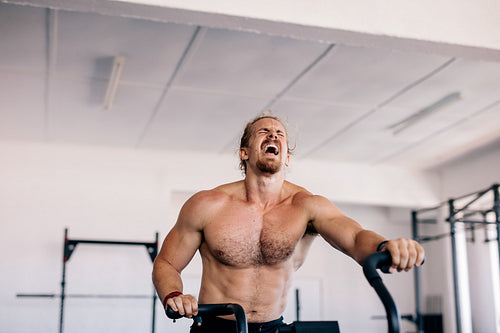 Muscular man doing intense workout on gym bike