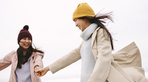 Happy asian woman in winter wear walking outdoors holding hands