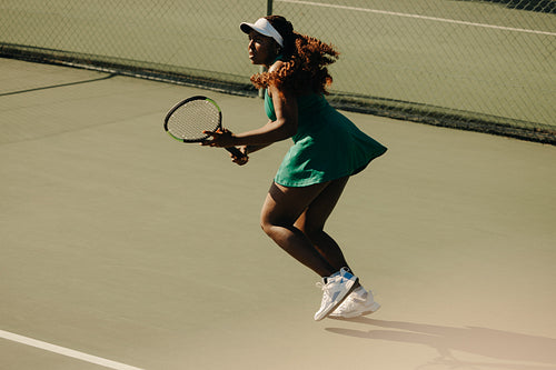 African-American woman running on tennis court during competition with long curly hair