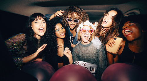 Group of girlfriends in the backseat of a taxi with festive accessories and joyful smiles