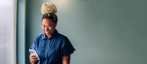 Woman using a smartphone while smiling near a teal wall