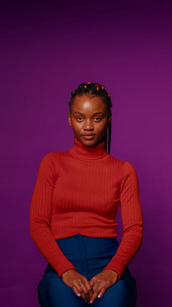 Young woman with braids sits calmly against a vibrant purple backdrop