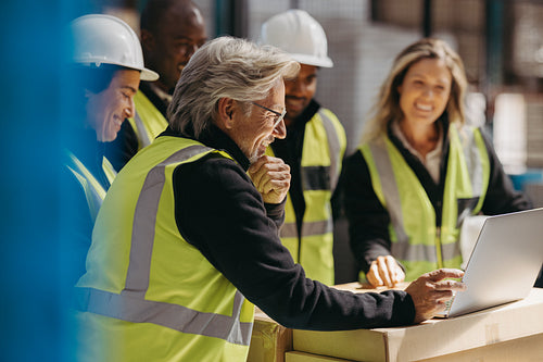 Smiling warehouse manager showing his team a presentation on a laptop