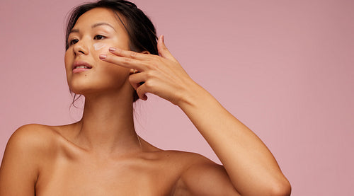 Asian woman applying anti-aging cream on her face