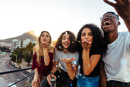 Friends blowing confetti at rooftop party