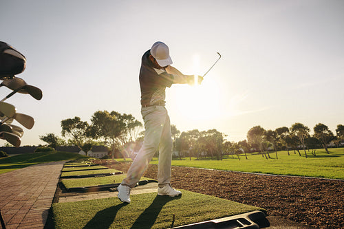 Professional golfer practicing his swing in the sunlight at a beautiful golf course