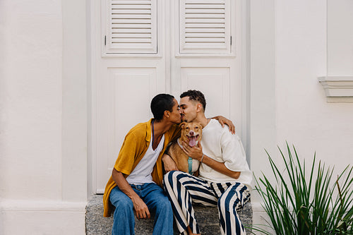 Couple sitting with dog, sharing affection outside a white building