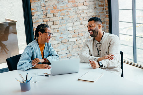 Smiling colleagues enjoying a productive corporate meeting in a well-lit and spacious office setting with a laptop and notes