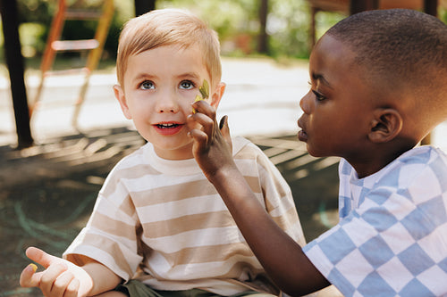 Children sharing a playful moment with face painting outdoors in a sunny park